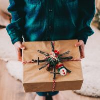 child holding a gift wrapped in brown paper with christmas decorations on top.