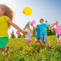 kids running on the grass with balloons on strings