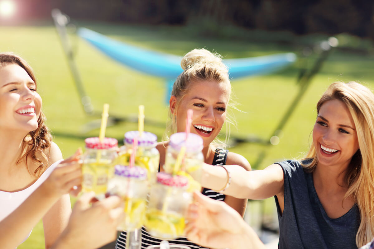 three women clinking their drinks together at a backyard bbq