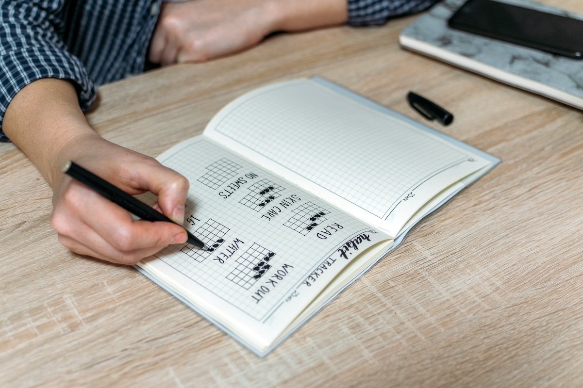 Bullet Journal, Habit Tracker. Female hand notes in habits tracker. Woman cross off day with routine in her Habit Tracker. Selective focus.