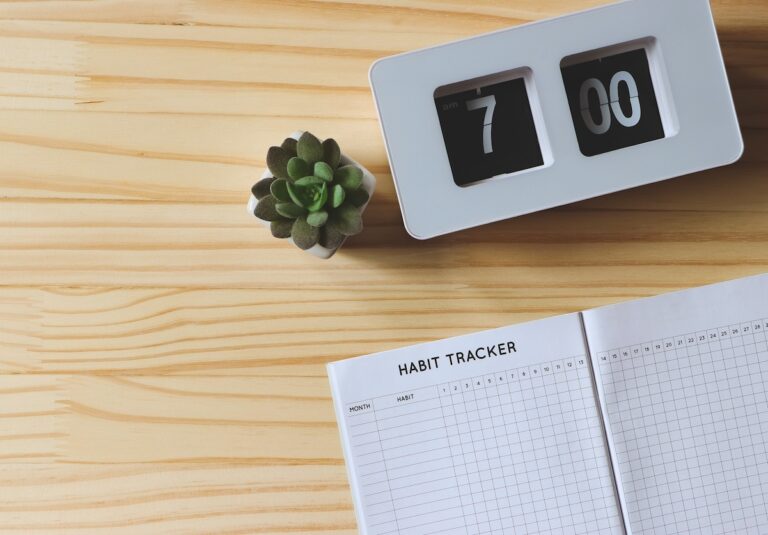 Top view or flat lay of habit tracker book, flip clock 7 am and succulent plant pot on wooden table background with copy space.