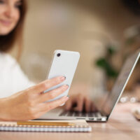 woman sitting at her desk with her laptop open and looking at her phone