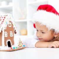 little girl with santa hat looking at gingerbread house