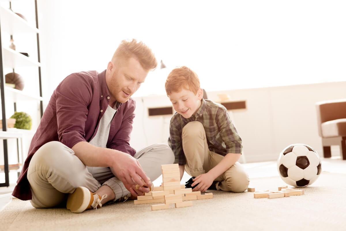 father and son sitting on the carpet playing a block building game