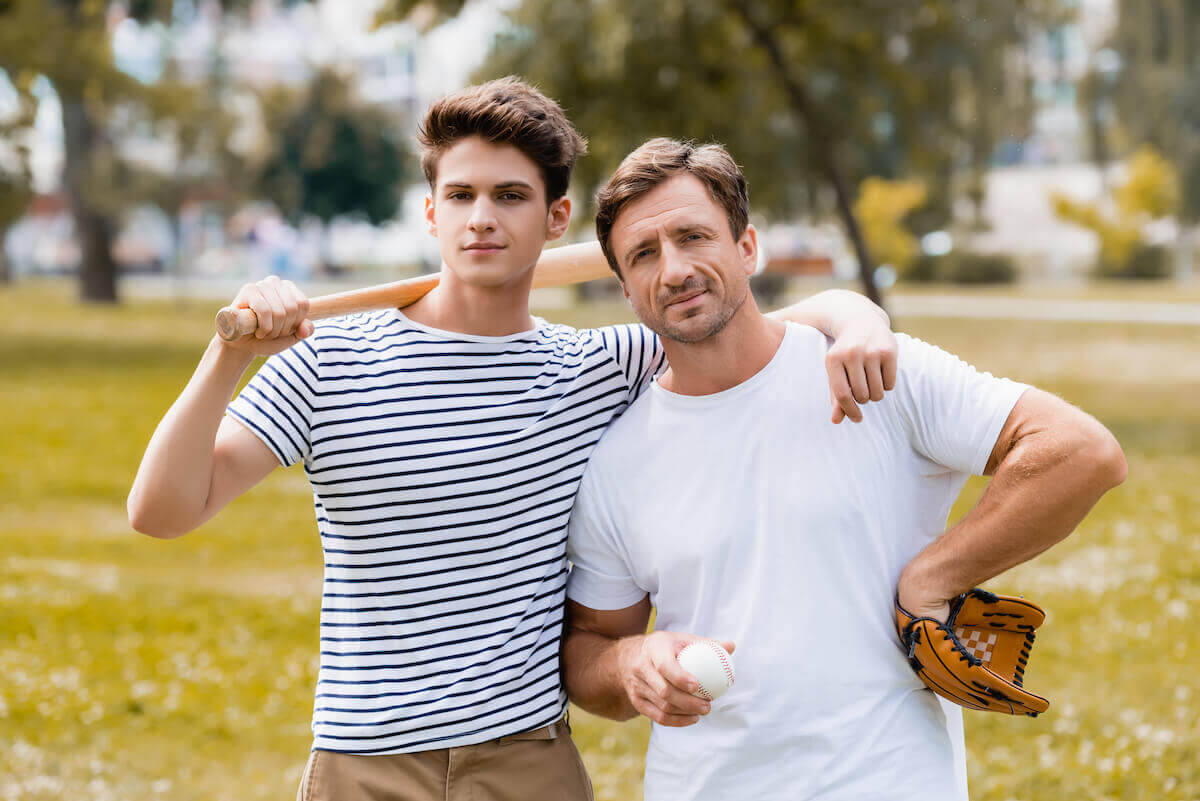 teenage son with arm around father holding a baseball bat