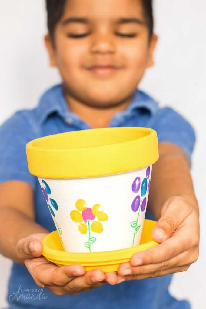 little boy holding out a terracotta pot plant that has been handpainted.