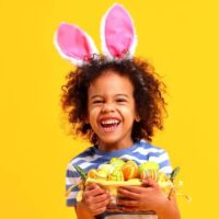 child with bunny ears and easter basket on yellow background