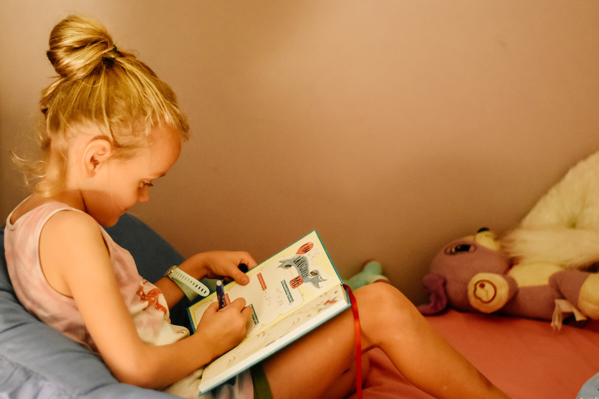 child filling in gratitude journal on her bed