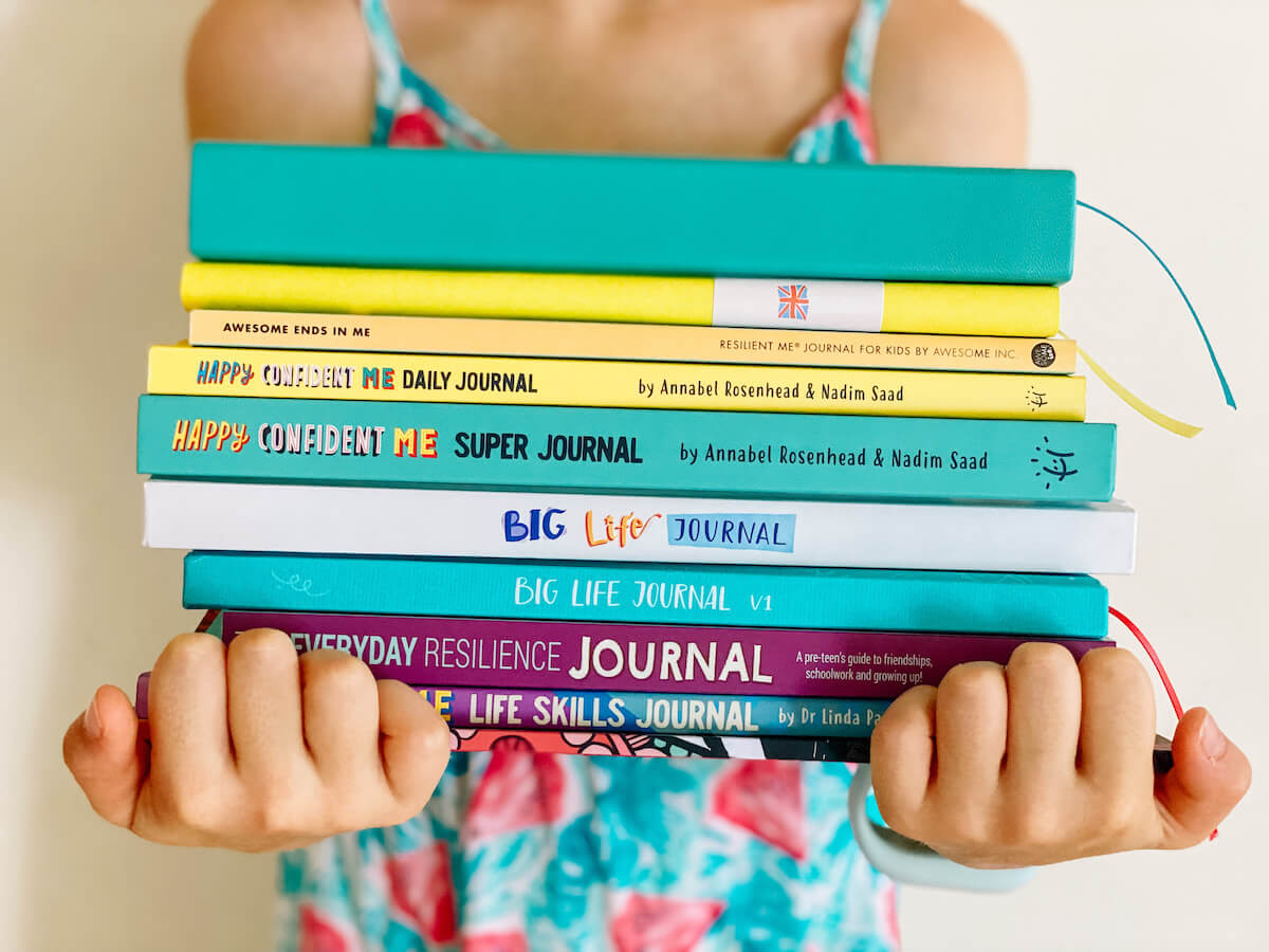 growth mindset and gratitude journals stacked in child's arms