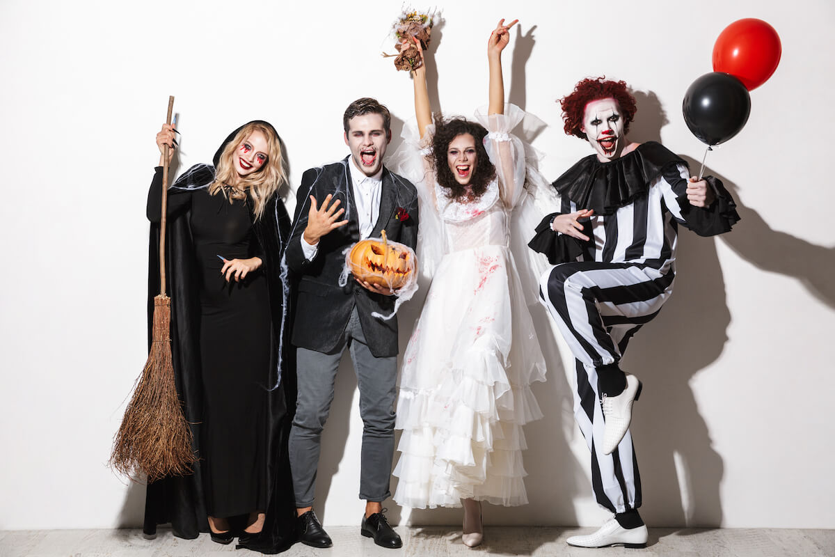 4 friends in fancy dress costumes at a halloween party including a witch, clown, bride and vampire