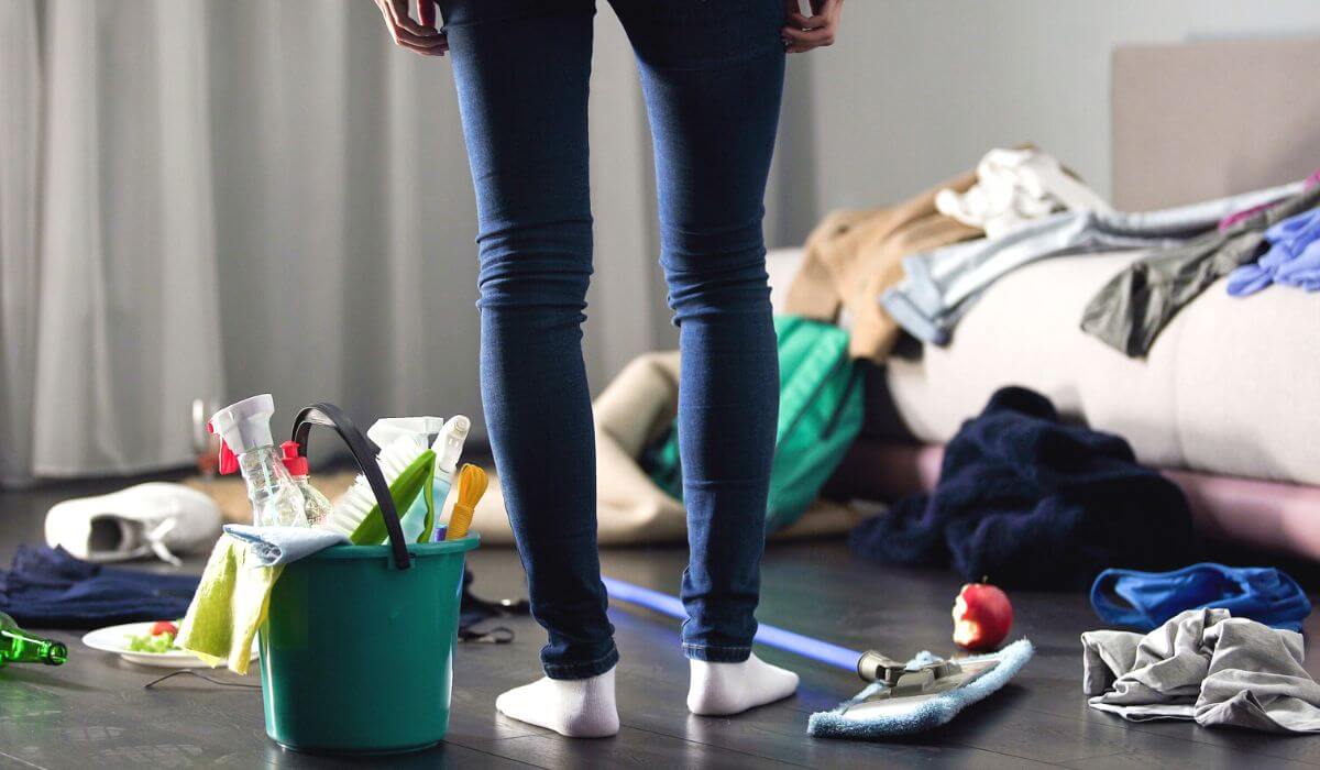 woman standing in front of a pile of mess with bucket of cleaning supplies