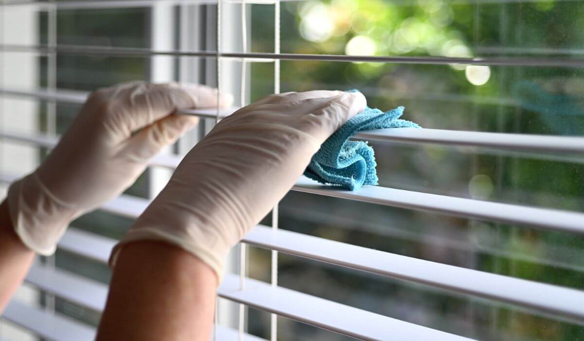 person wearing rubber gloves cleaning vertical blinds