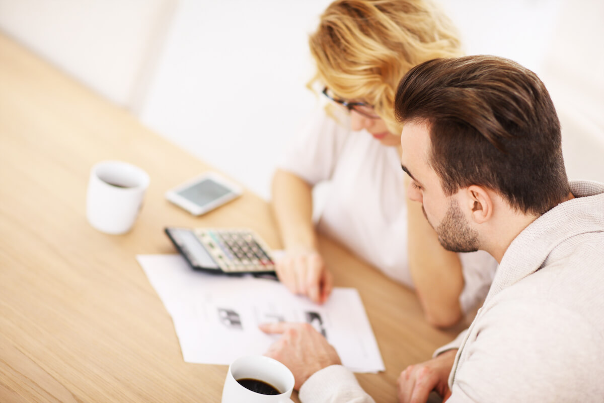 man and woman at dining table with calculator and paperwork preparing a household budget