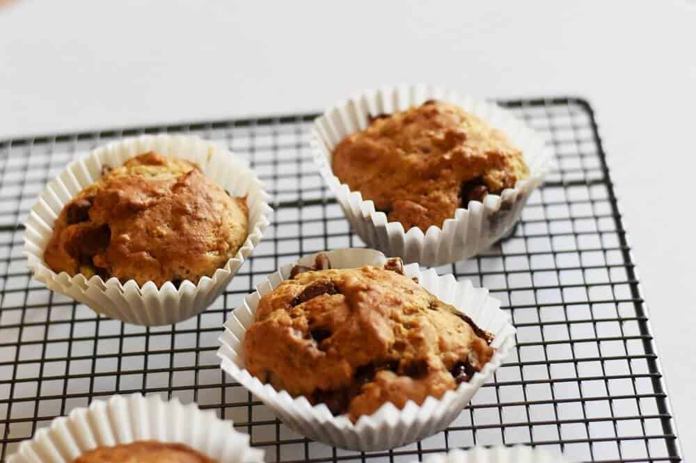 Banana choc chip muffins in cupcake pans on a cooling rack.