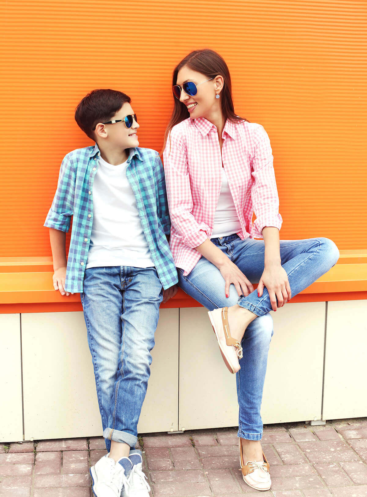 mother and son with sunglasses on sitting on a bench in front of a bright orange wall