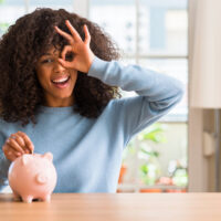 woman in a blue shirt putting a coin in a piggy bank