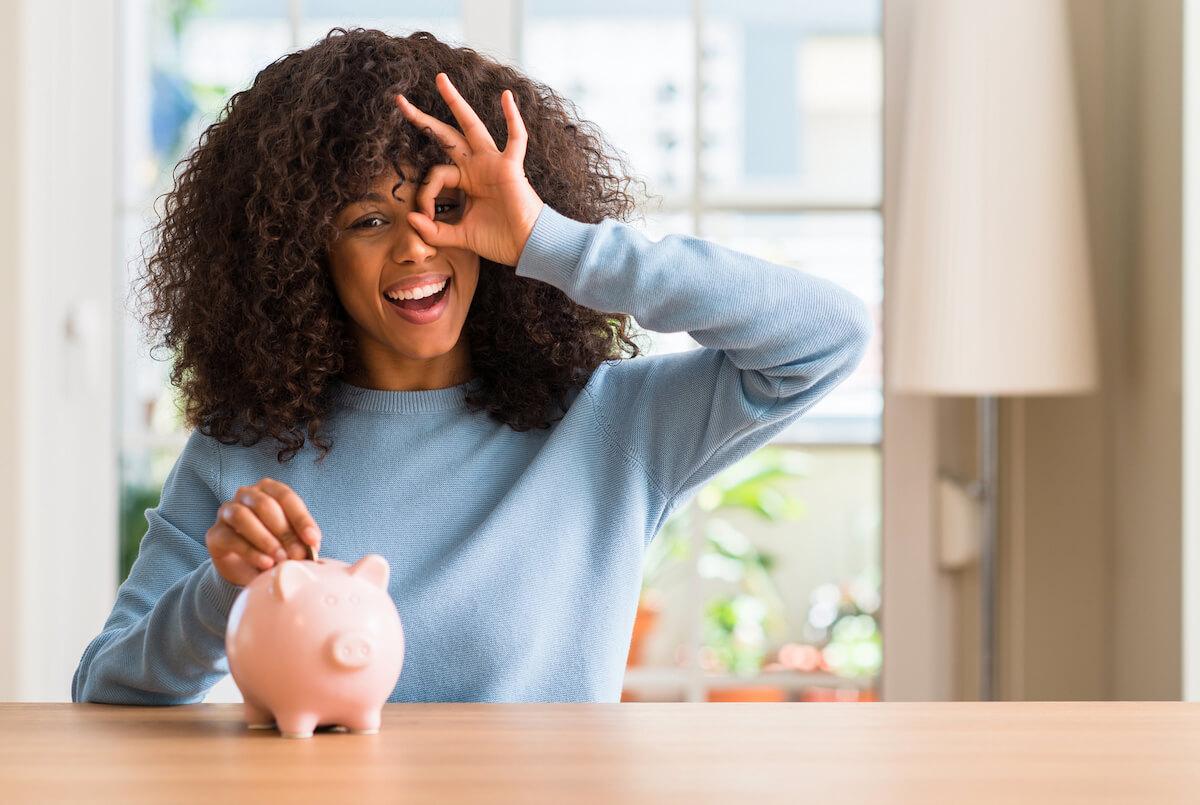 woman in a blue shirt putting a coin in a piggy bank