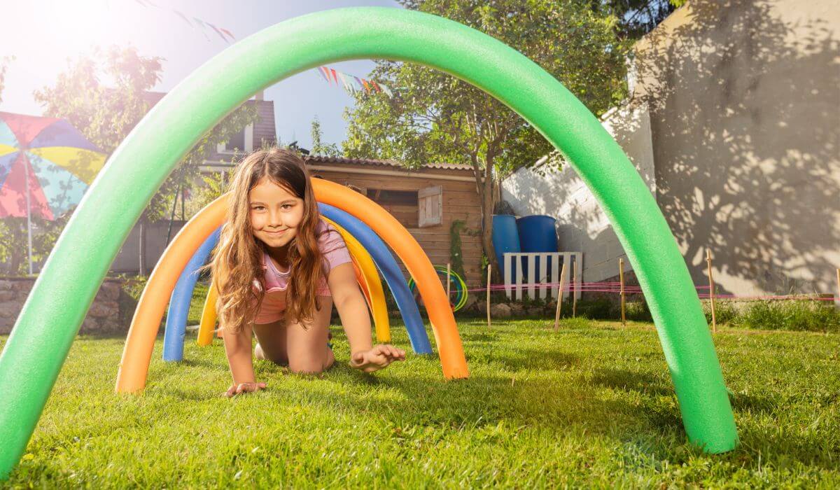 young girl crawling under pool noodle tunnel