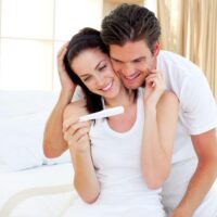 a couple excited looking at a positive pregnancy test while sitting on their bed