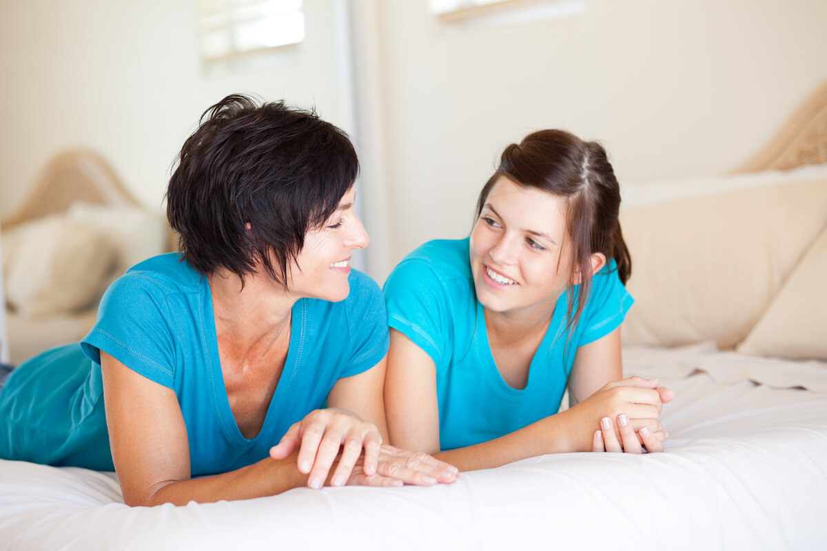 mother and daughter lying on bed talking together in blue shirts