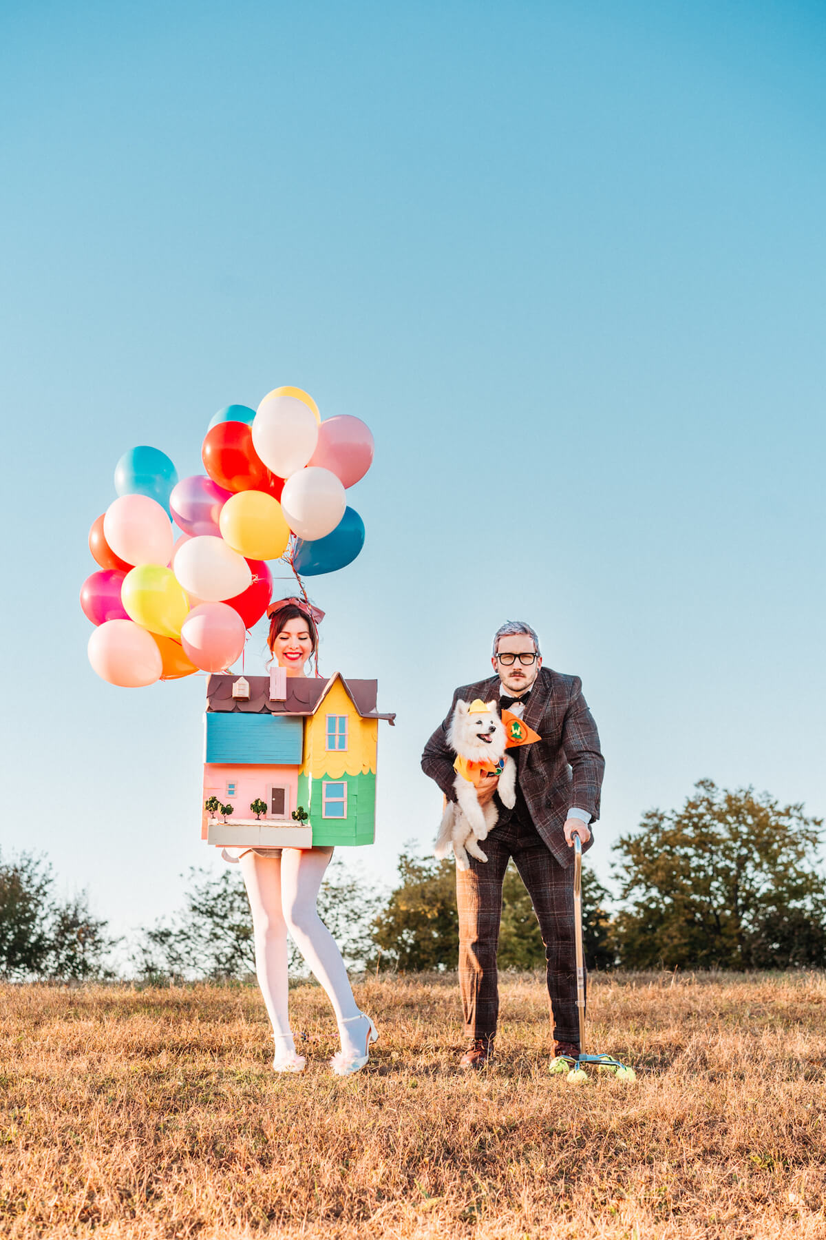 DIY pixar up halloween costume with woman dressed as house with balloons and man dressed as carl with their dog dressed as russell