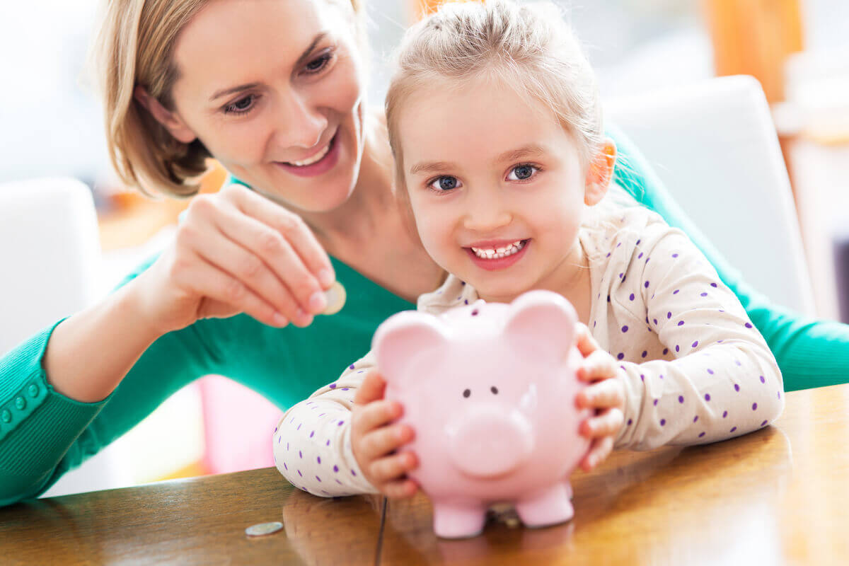 young girl holding her piggy bank while woman is about to put a coin inside