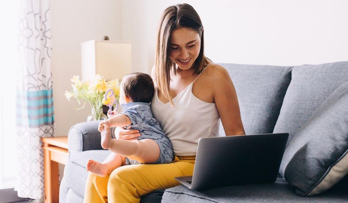 woman holding her baby in her lap while working on her laptop