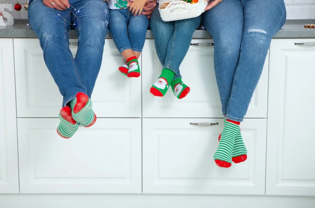 family sitting on a kitchen counter each wearing blue jeans and christmas socks