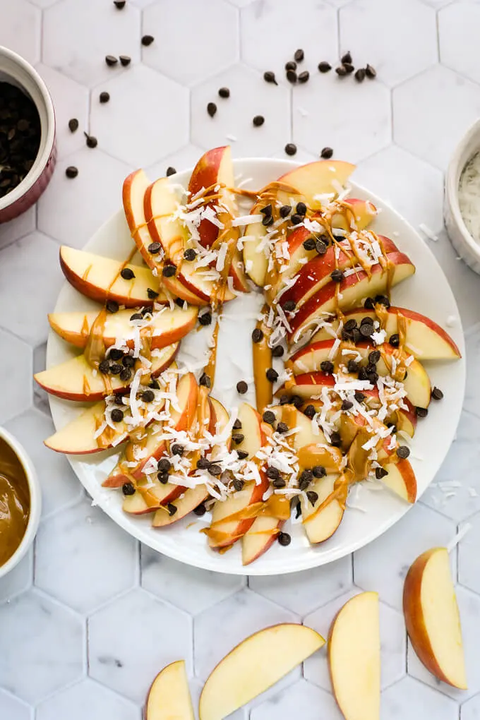 large white plate with apple nachos with chocolate chips, coconut and peanut butter drizzle