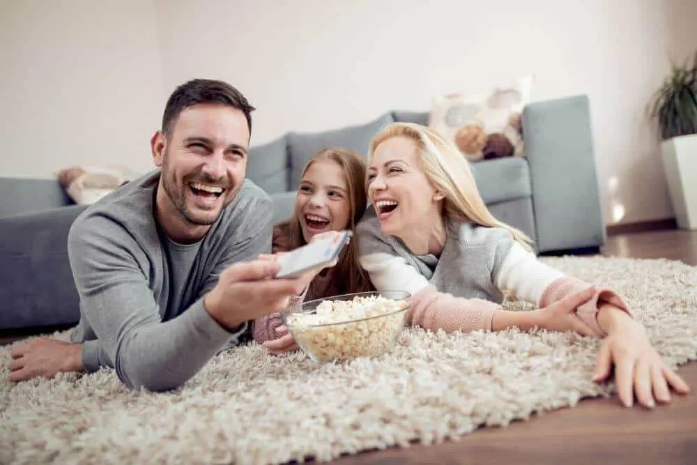 family movie night with family on floor of living room with bowl of popcorn. 