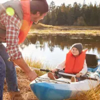 father pushing blue kayak into water with young son sitting in kayak