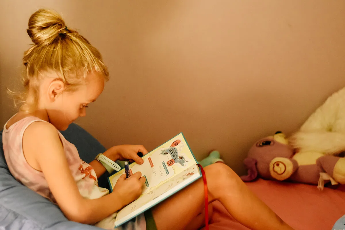 child filling in gratitude journal on her bed