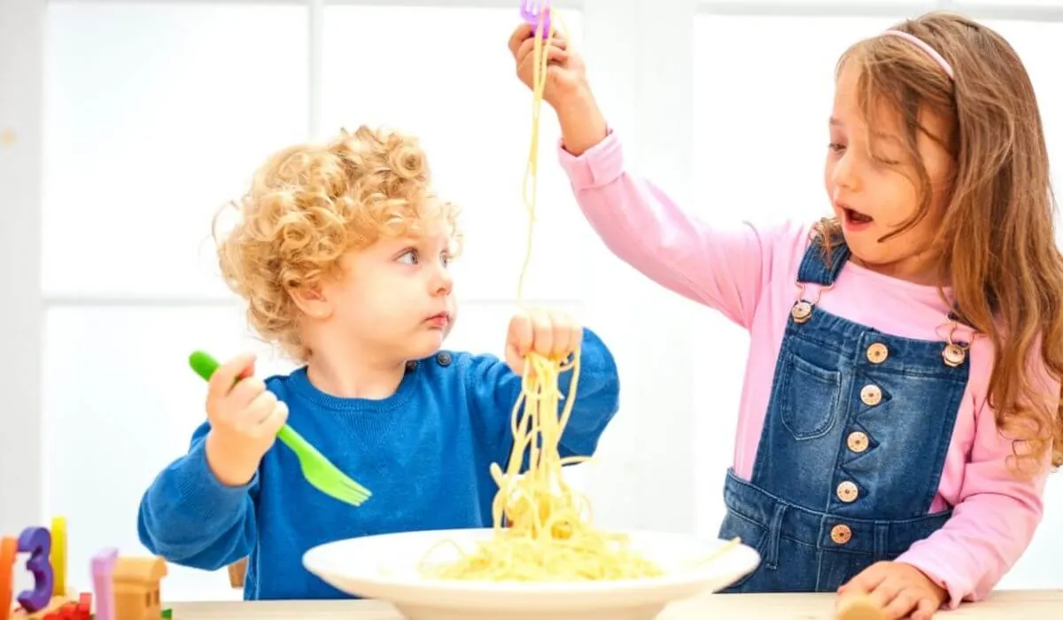 two kids eating plain spaghetti from a bowl