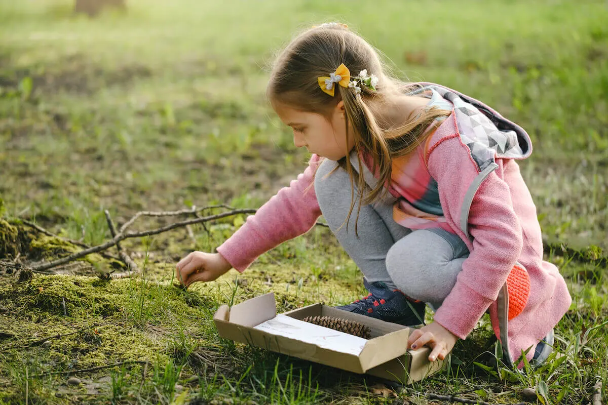 child collecting items to put in a box during a nature scavenger hunt