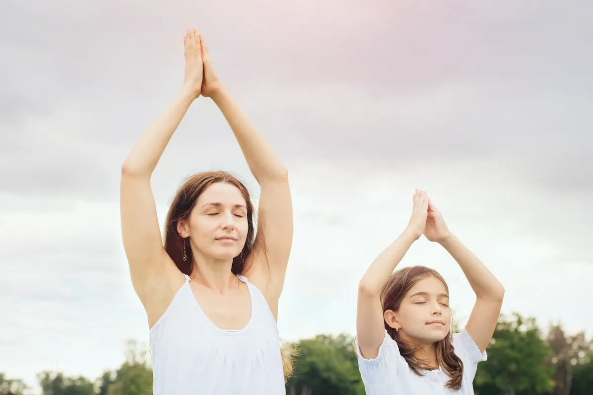 Young mother and daughter meditating and doing yoga exercise in the city park