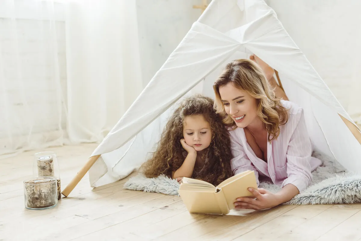 mother and daughter reading a book in a play tent