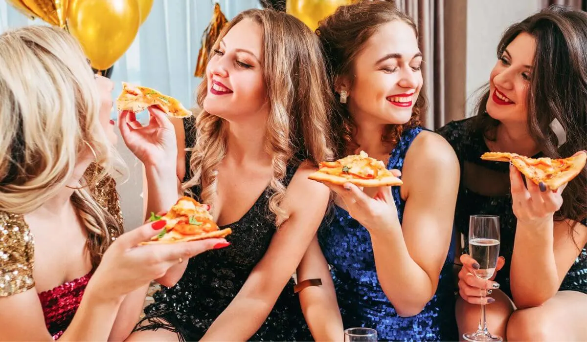 a group of women at a party eating pizza and drinking champagne