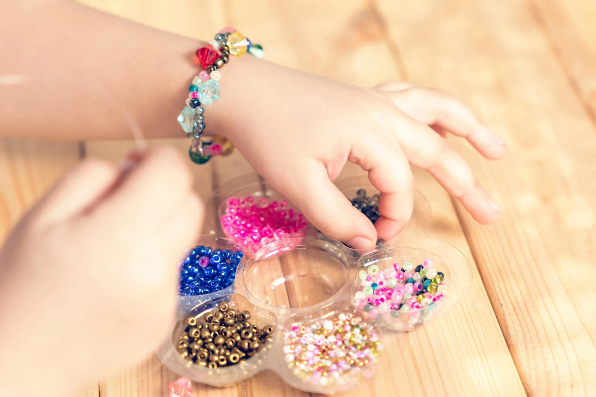 child with tray of beads making beaded bracelets on a wooden table