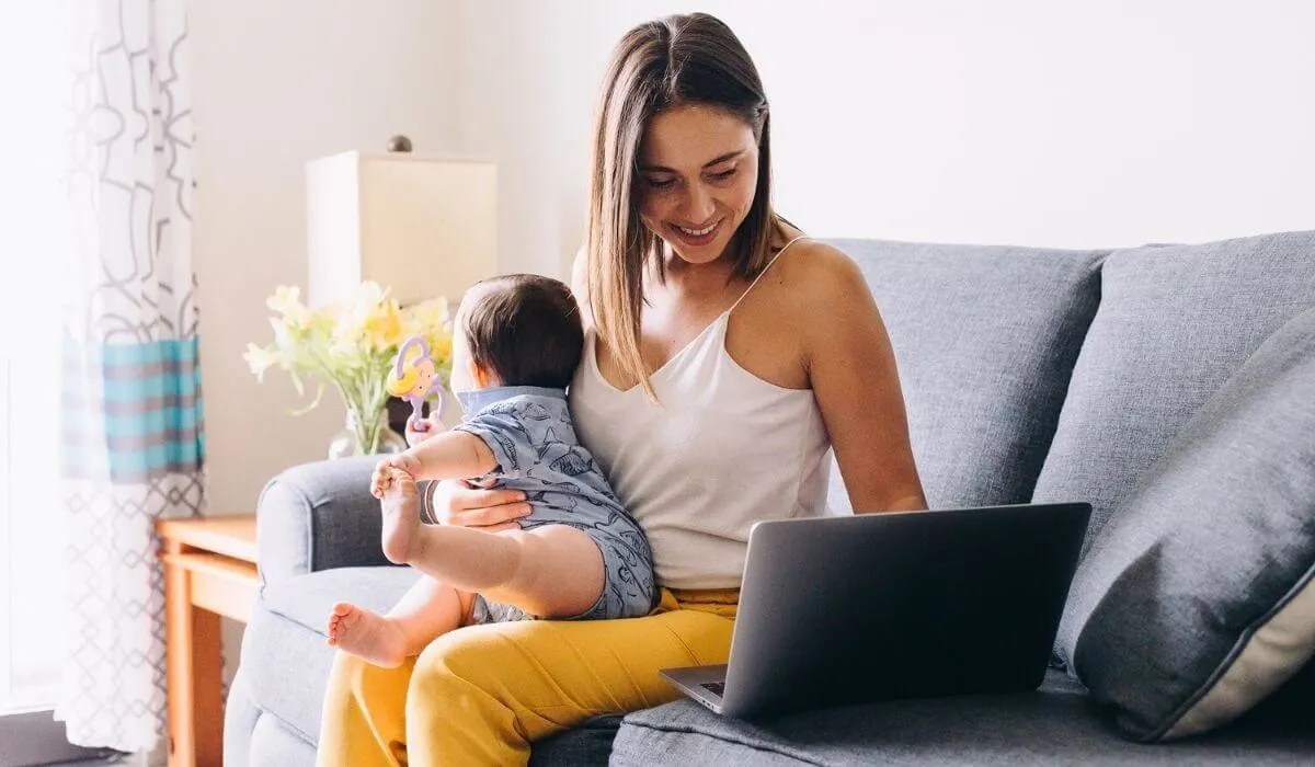 woman holding her baby in her lap while working on her laptop